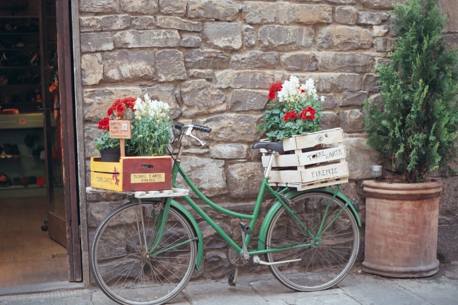 Bici verde con cestini di fiori contro muro di pietra toscano
