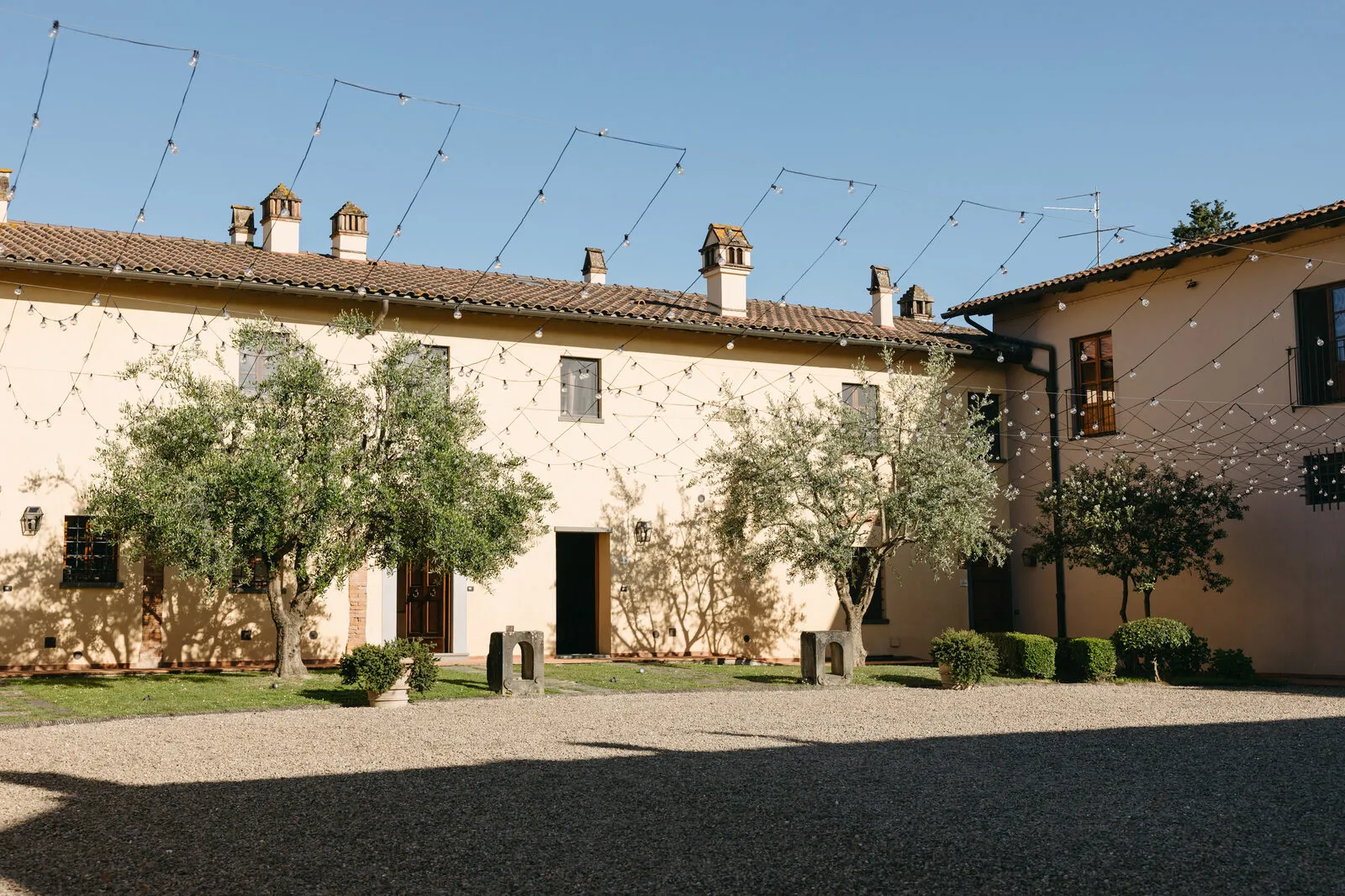Cortile del casolare toscano con ulivi, ghiaia e facciata color crema